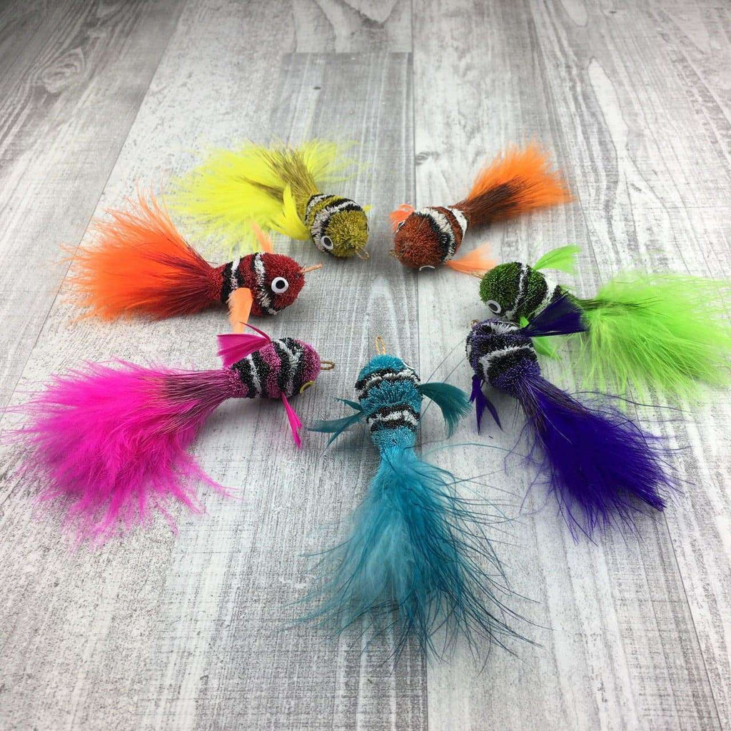 These are an assortment of Pretty Fly Clownfish Teaser Wand Cat Toy Replacement Lures by Catboutique. They are orange, burnt orange-red, green, purple, light blue, yellow, hot pink, and neon green. They are made out of deer hair and have feather tails. Each lure is colored with a dye that isn't harmful to cats. This lure is meant to engage at the cat's hunting instincts like prowling, pawing, and pouncing.