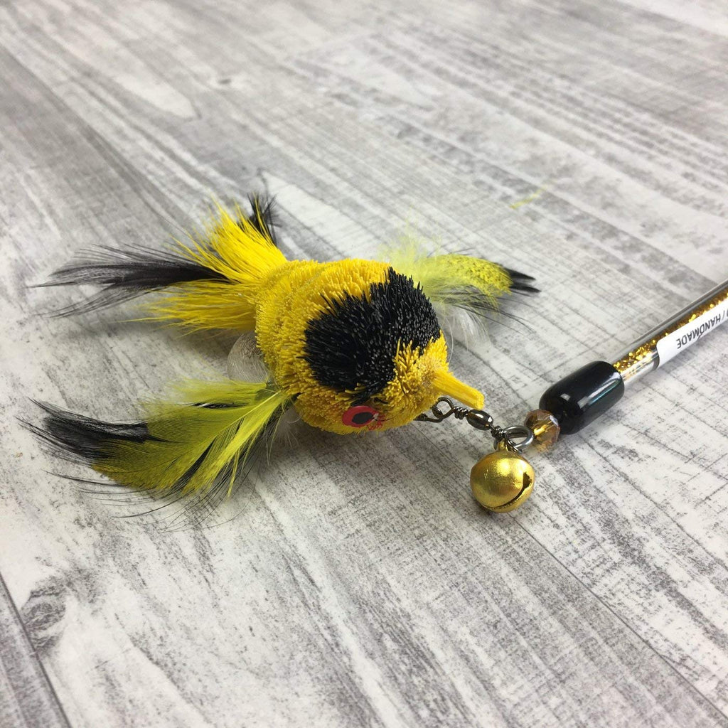This is a Pretty Fly Bird Teaser Wand Cat Toy Replacement Lure by Catboutique. The bird is made from real deer hair and it gives a bristly hair appearance. It has bird feather for wings and a tail. There is a cotter ring clip where the beak should be. The bird is yellow mostly with a large black spot underneath the eyes. The bird has feathers for a tail and wings. This lure is meant to engage at the cat's hunting instincts like prowling, pawing, and pouncing. The lure works best with a teaser wand cat toy. 