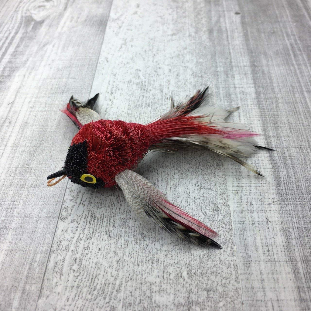 This is a Pretty Fly Bird Teaser Wand Cat Toy Replacement Lure by Catboutique. The bird is made from real deer hair and it gives a bristly hair appearance. It has bird feather for wings and a tail. There is a cotter ring clip where the beak should be. The bird is mostly red and has a black spot underneath the eyes at the front of the face. There is a cotter ring clip where the beak should be. This lure is meant to engage at the cat's hunting instincts like prowling, pawing, and pouncing.